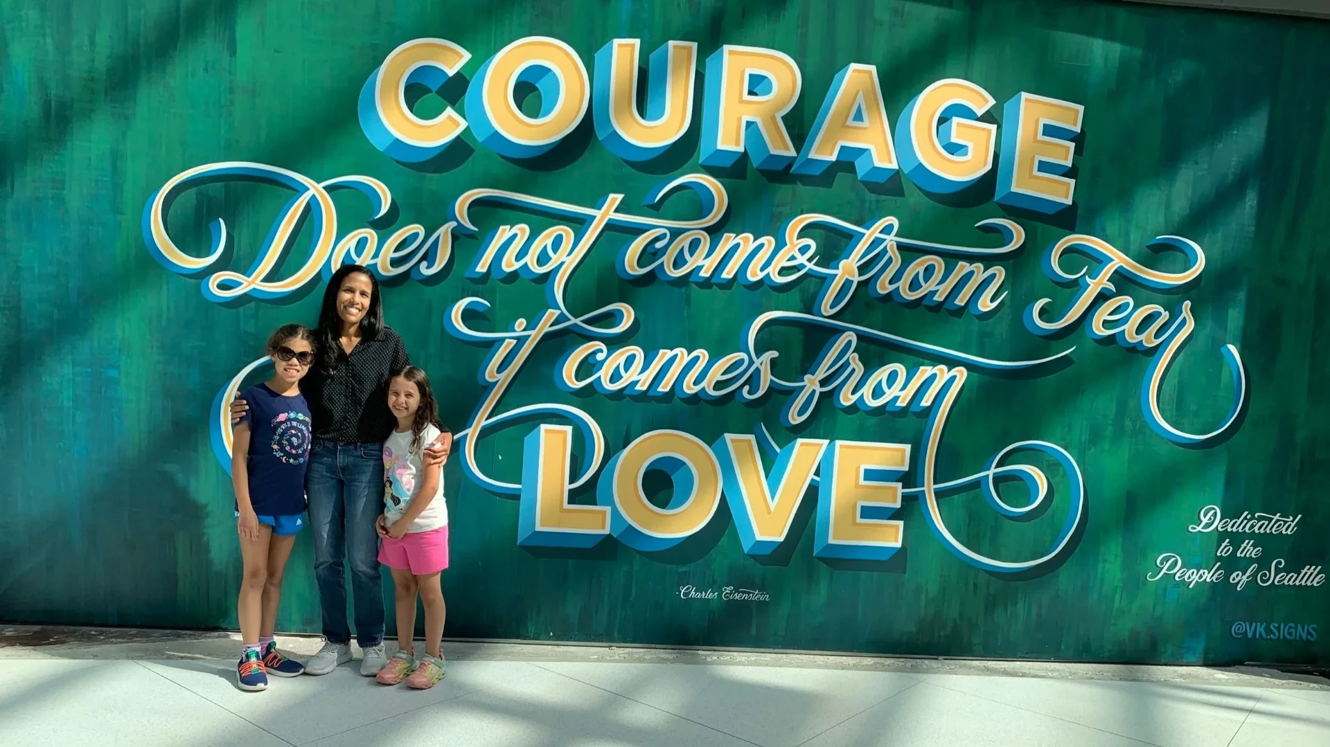 Briana Woods-Jaeger and her daughters standing in front of a colorful Courage mural